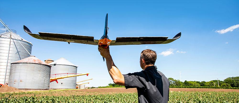 一名男子站在农田附近，准备从右手发射一架固定翼无人机